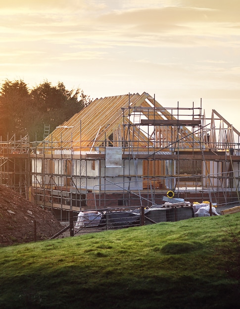 Maison en construction: Charpente en bois et échafaudages Maison en construction au lever du soleil, avec charpente en bois et échafaudages. Pelouse verte au premier plan.