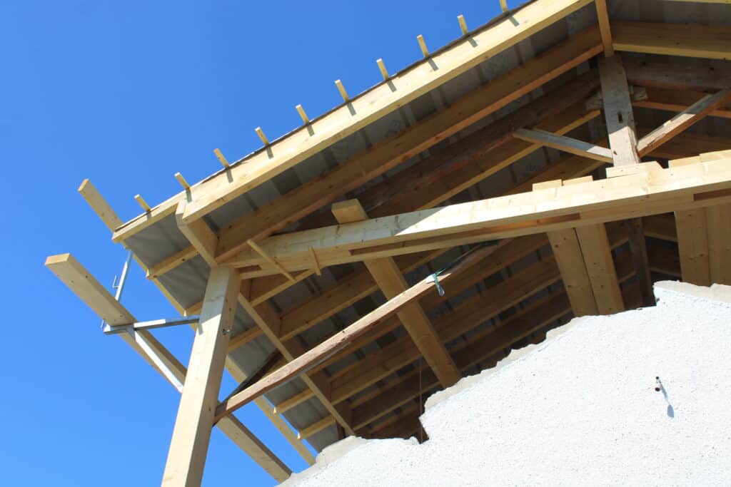 Construction de toit : charpente bois et ciel d'été Charpente de toit en bois en construction vue de dessous sous un ciel bleu. Poutres, chevrons et membrane sont visibles.