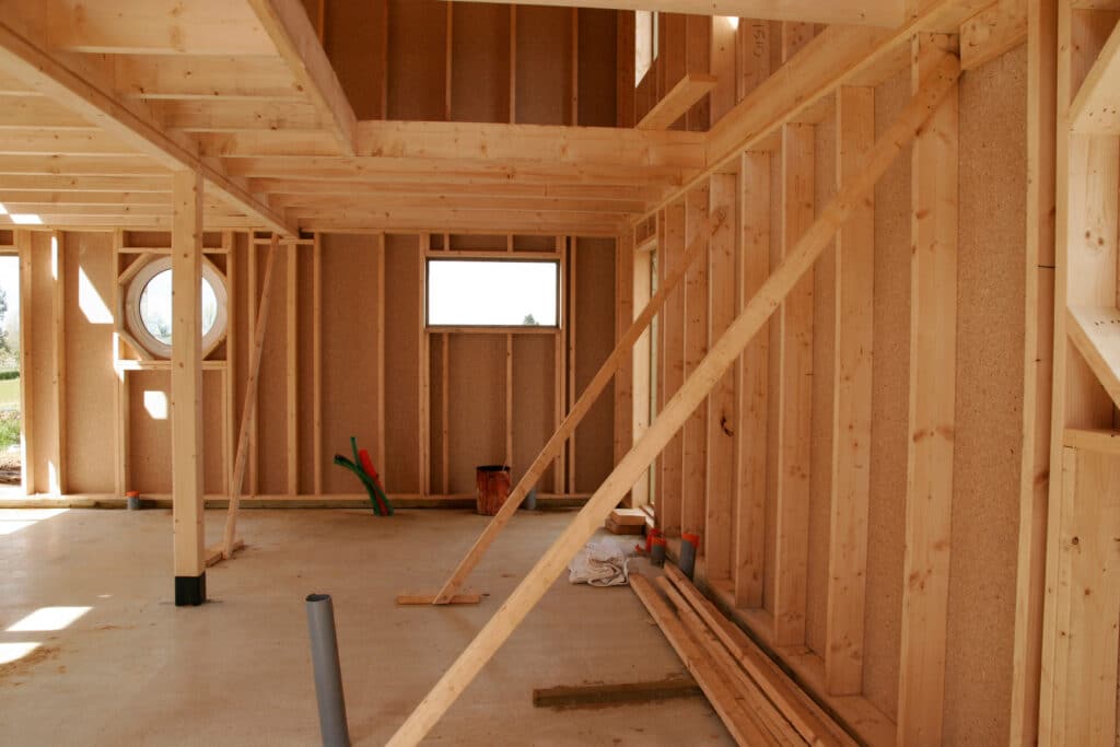 Construction maison ossature bois : intérieur brut et lumineux Intérieur d'une maison en construction, avec l'ossature bois et les panneaux OSB apparents. Fenêtres ronde et rectangulaire, sol en béton.