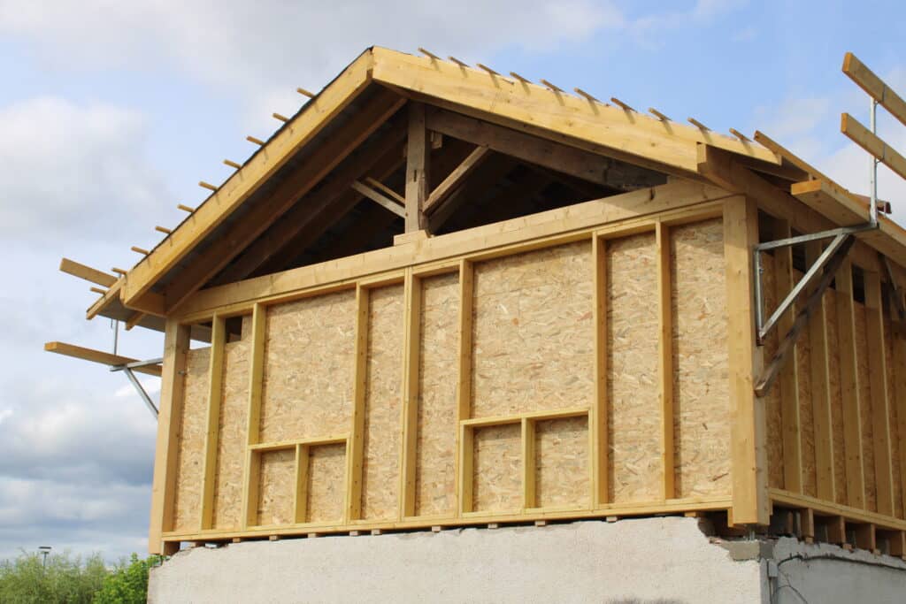 Maison en Construction : Ossature Bois et Panneaux OSB Maison en construction à ossature bois avec murs en panneaux OSB et charpente apparente. Toit en cours sous ciel nuageux.
